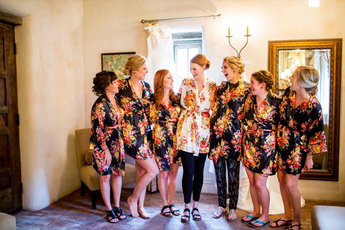 Bride and six bridesmaids in floral robes laughing together in the getting-ready suite