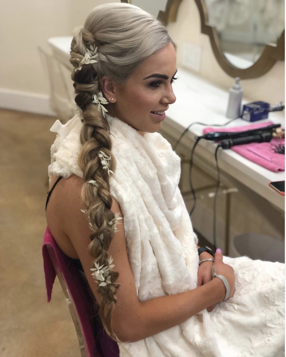 Bride in a white robe with a long side braid woven with greenery, getting ready in the salon