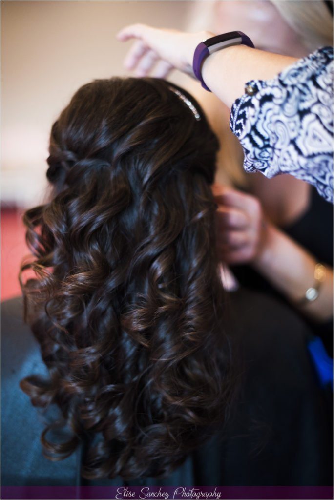 A Chairish the Day stylist's hands finishing long dark curls on a bride, photographed from behind